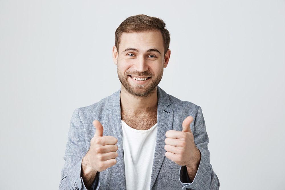 Smiling man giving a double thumbs-up gesture, exuding confidence and positivity.